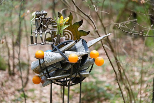 Detailed metal sculpture with orange spheres and figures in a tranquil forest.