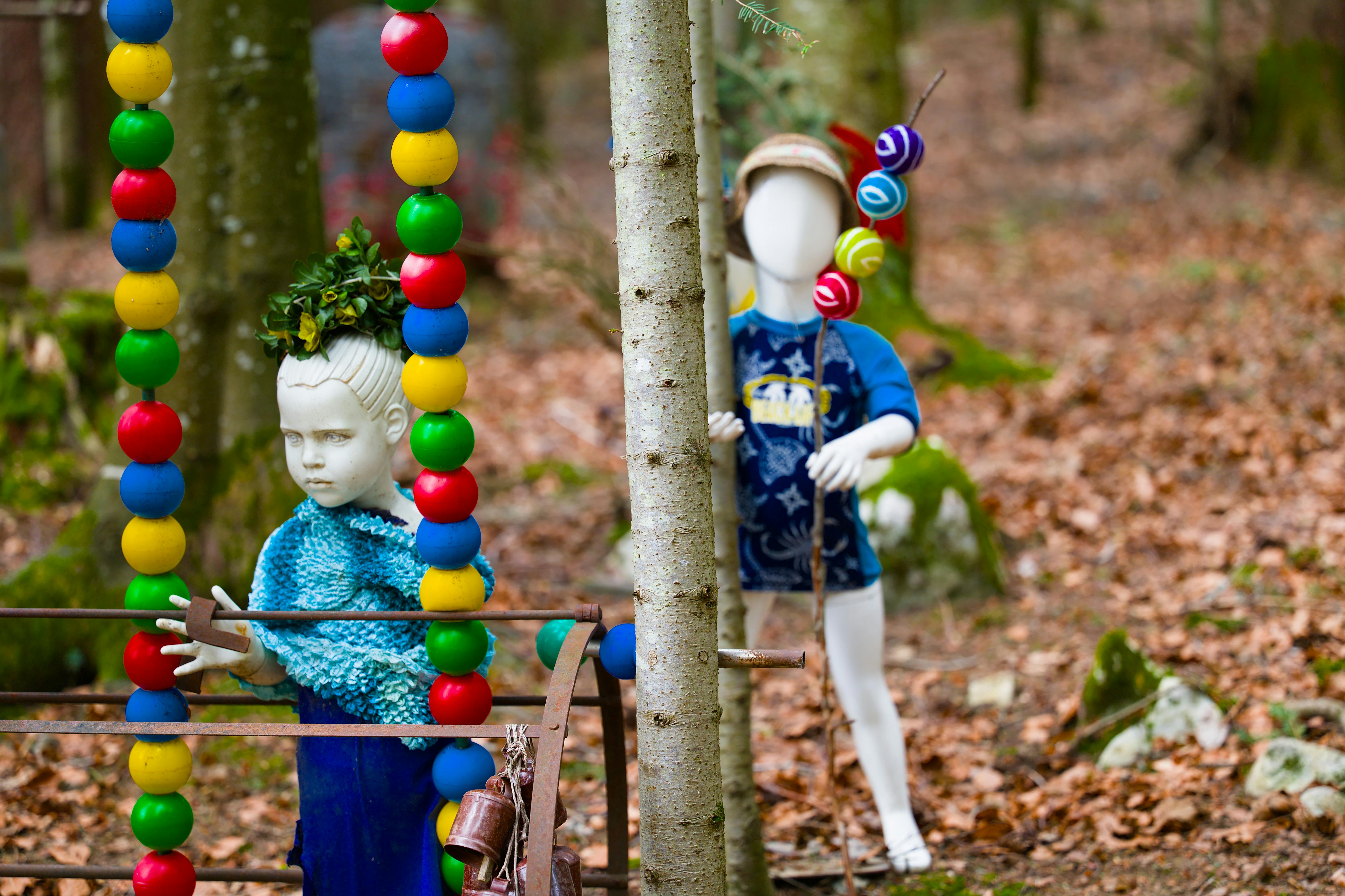 Des mannequins colorés mis en scène de façon artistique au milieu d'arbres ornés de perles éclatantes lors d'une exposition en forêt.