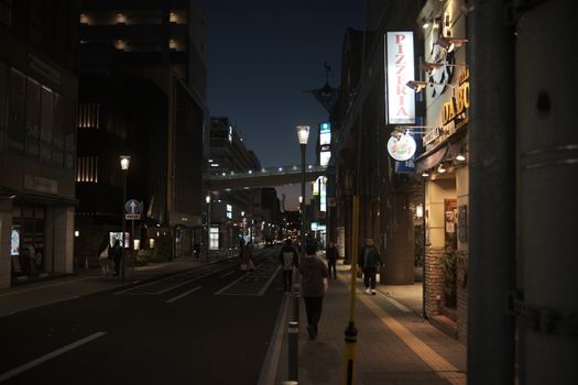 Urban night scene with illuminated street signs and people walking in a city setting under streetlights.