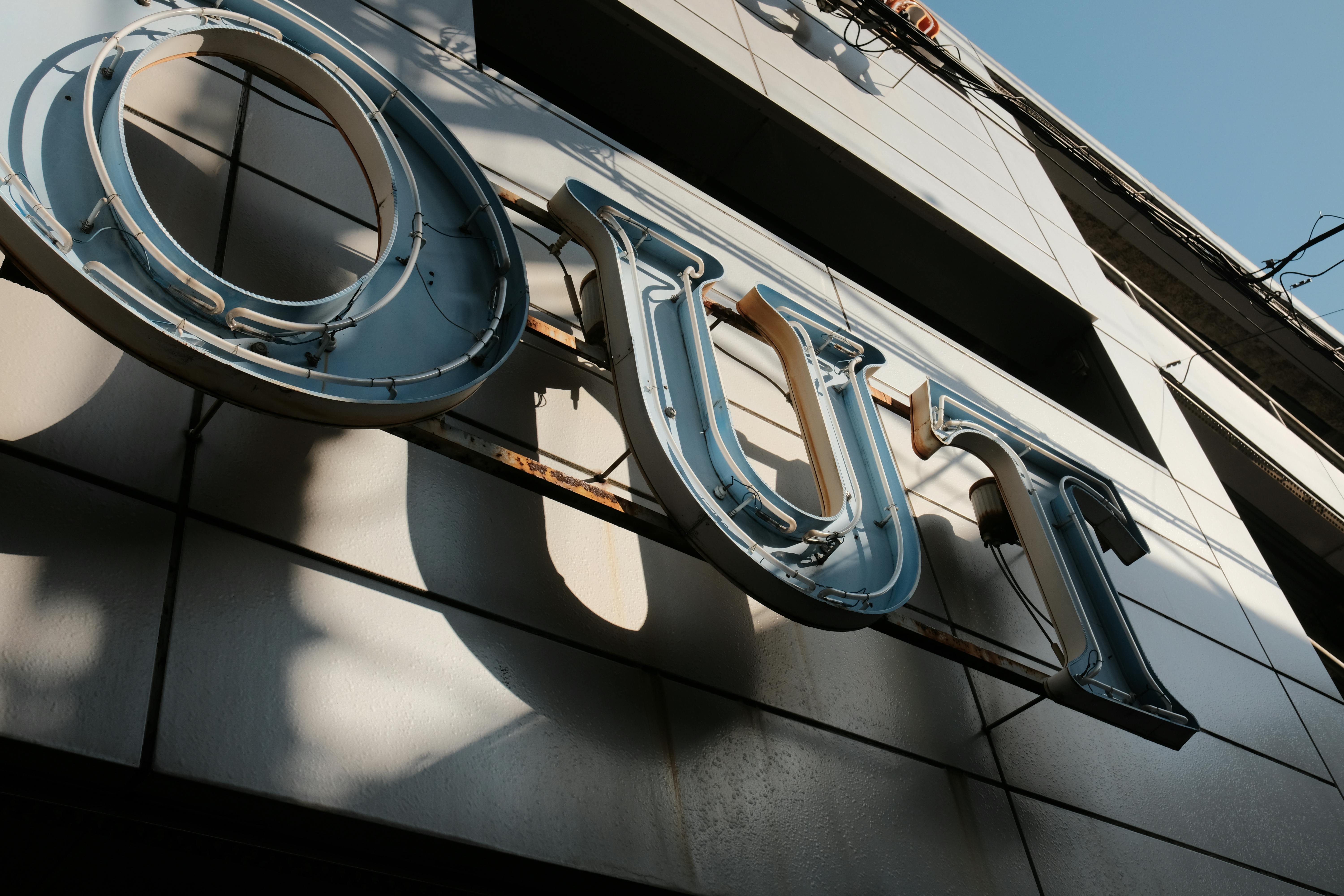 Low angle view of a neon sign reading 'OUT' against an urban building facade in daylight.