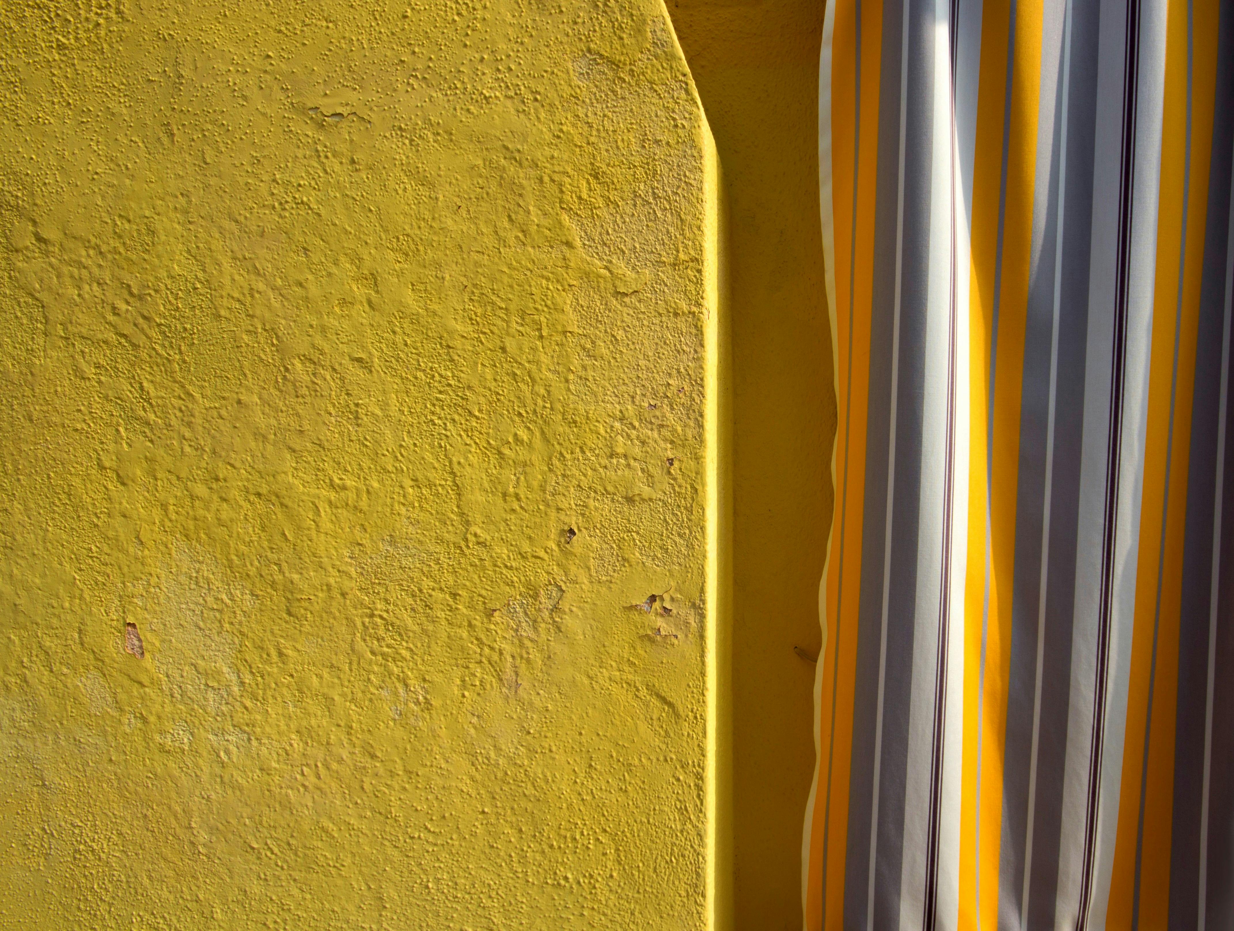 Close-up of a textured yellow wall with a striped curtain in Burano, Italy.