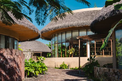 Free Charming tropical resort architecture with lush greenery and thatched roofs under a clear blue sky. Stock Photo