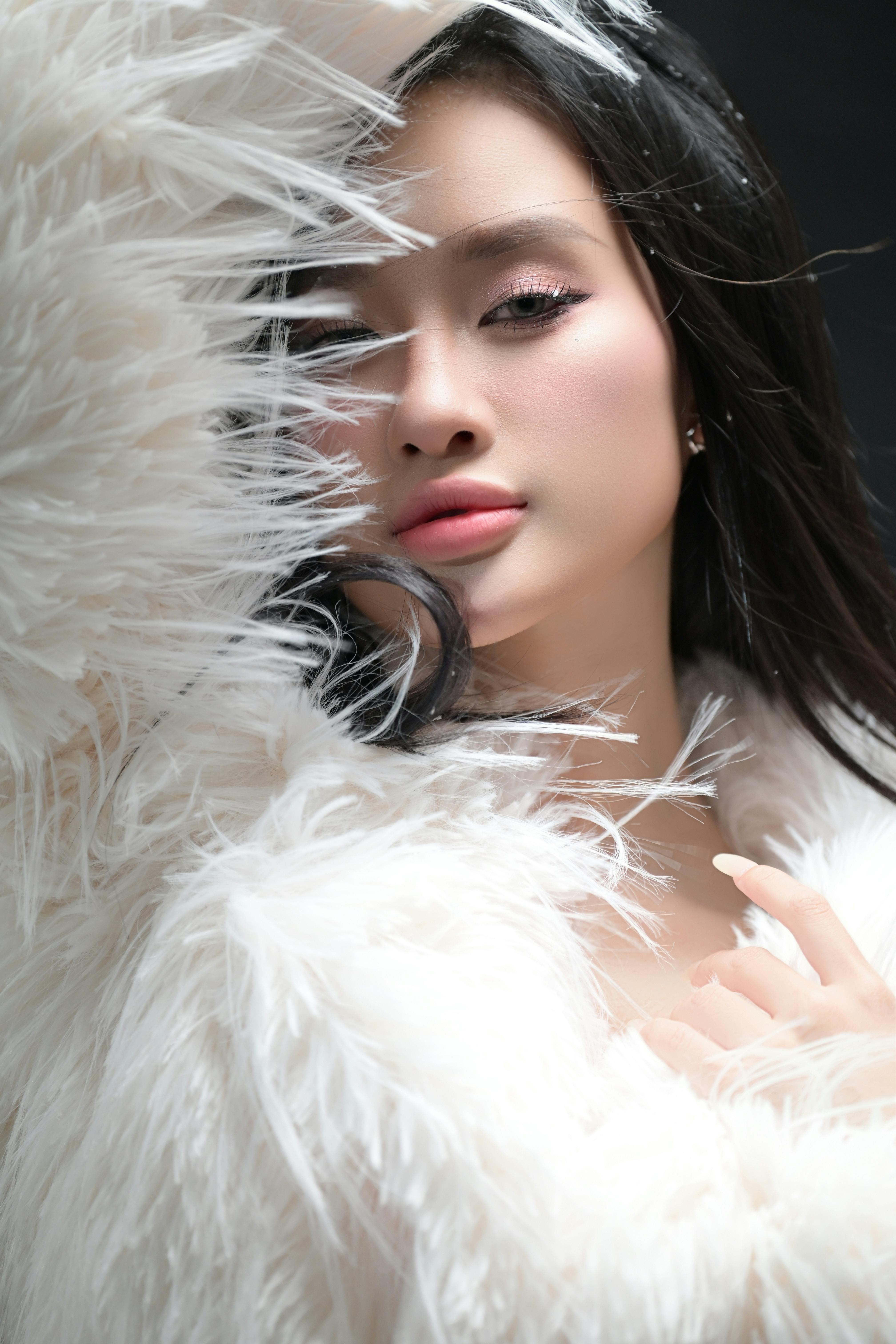 Fashion portrait of a young woman in a stylish white feathered coat against a dark background.