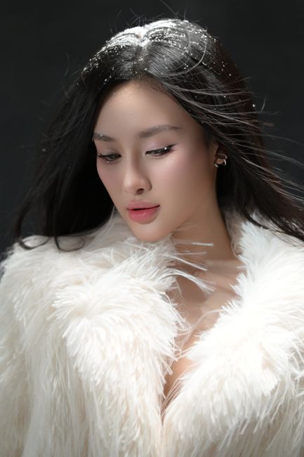 Portrait of a woman in a white fur coat with snowflakes in hair, exuding elegance.
