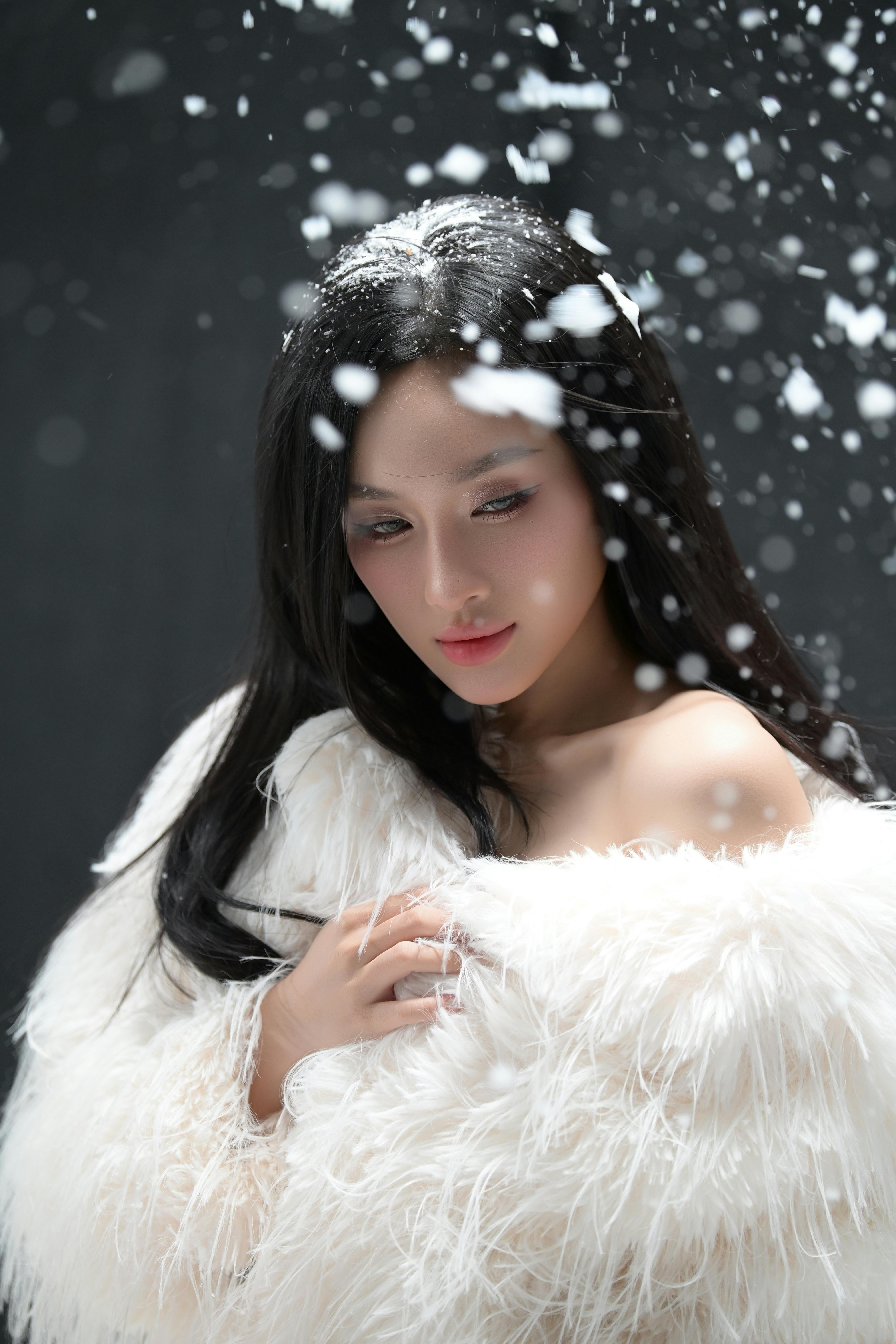 Portrait of a woman in a white fur coat with snowfall creating a magical effect.