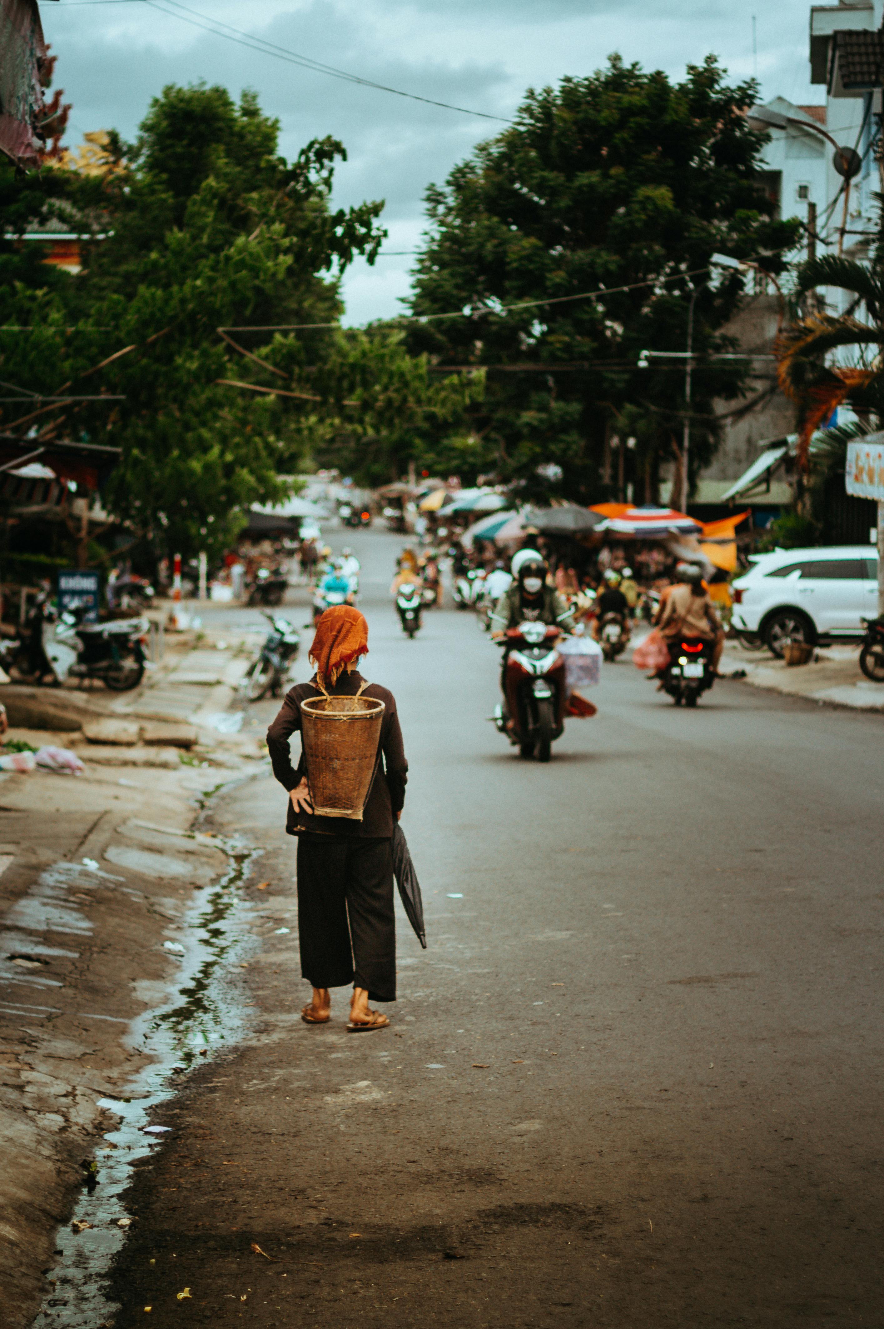 A woman in traditional attire walks on a bustling street in Kon Tum, Vietnam.