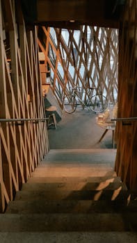 A modern indoor staircase with wooden lattice design leading to a cozy urban space with a bicycle.