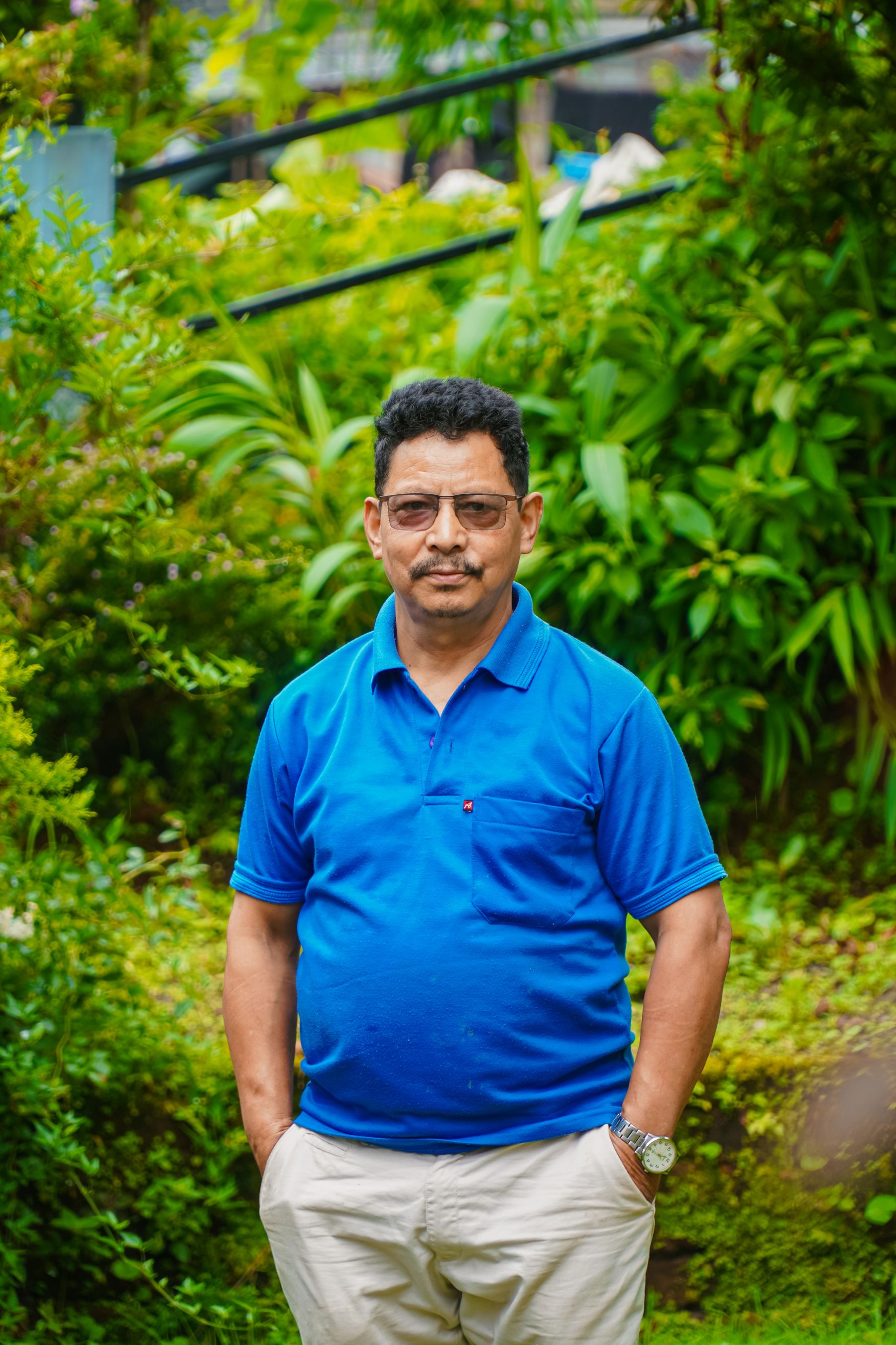 Middle-aged Indian man in a blue shirt and full-length trousers standing in a green garden for a sustainable weight-management story