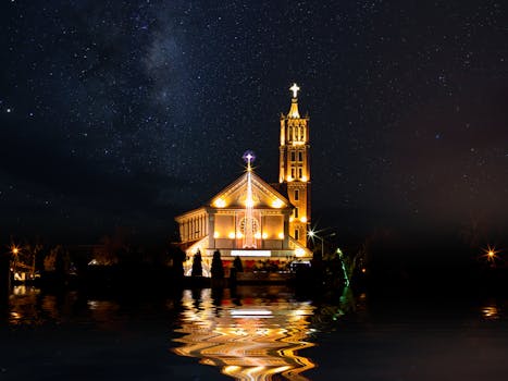 Beautifully lit church by night reflecting on water with a starry sky in Kon Tum, Vietnam.
