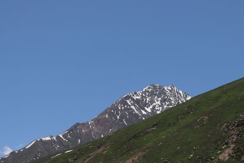 Free Snow-capped mountain peak with green slopes and clear blue sky, capturing a serene natural landscape. Stock Photo