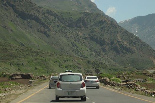 Cars driving through a lush mountain road under a clear blue sky, capturing a natural scenic view.