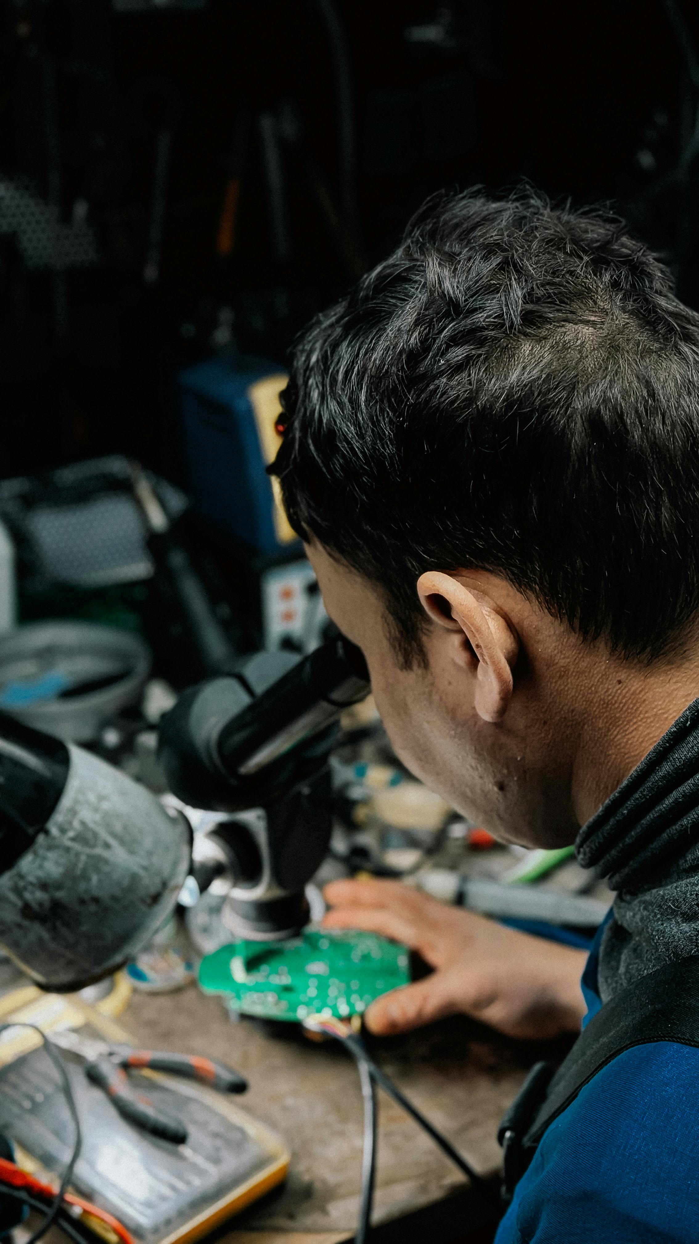 Technician examines a circuit board under a microscope, focused on precision electronics.