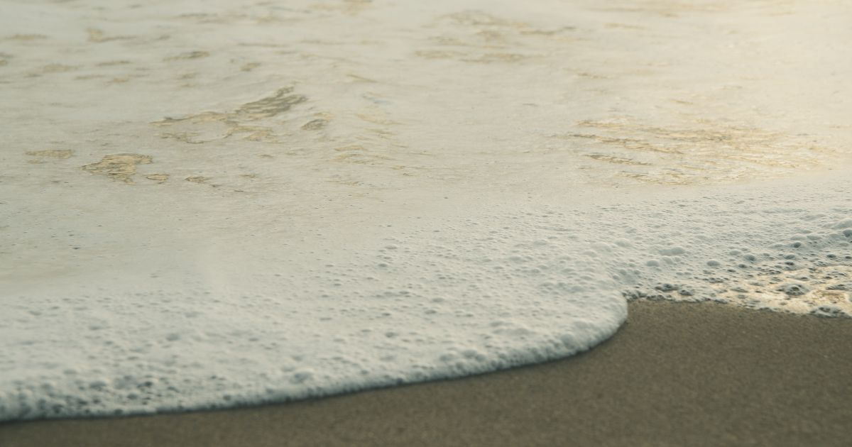 A wave washing over sand and receding, representing a liquidity sweep clearing a level before price reverses