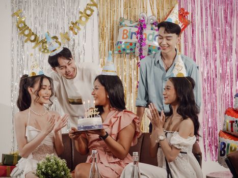 Group of friends celebrating a birthday with a cake, party hats, and decorations indoors.