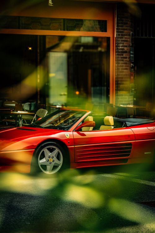 бесплатная Красный Ferrari припаркован возле городского кафе в окружении зелени. Стоковое фото