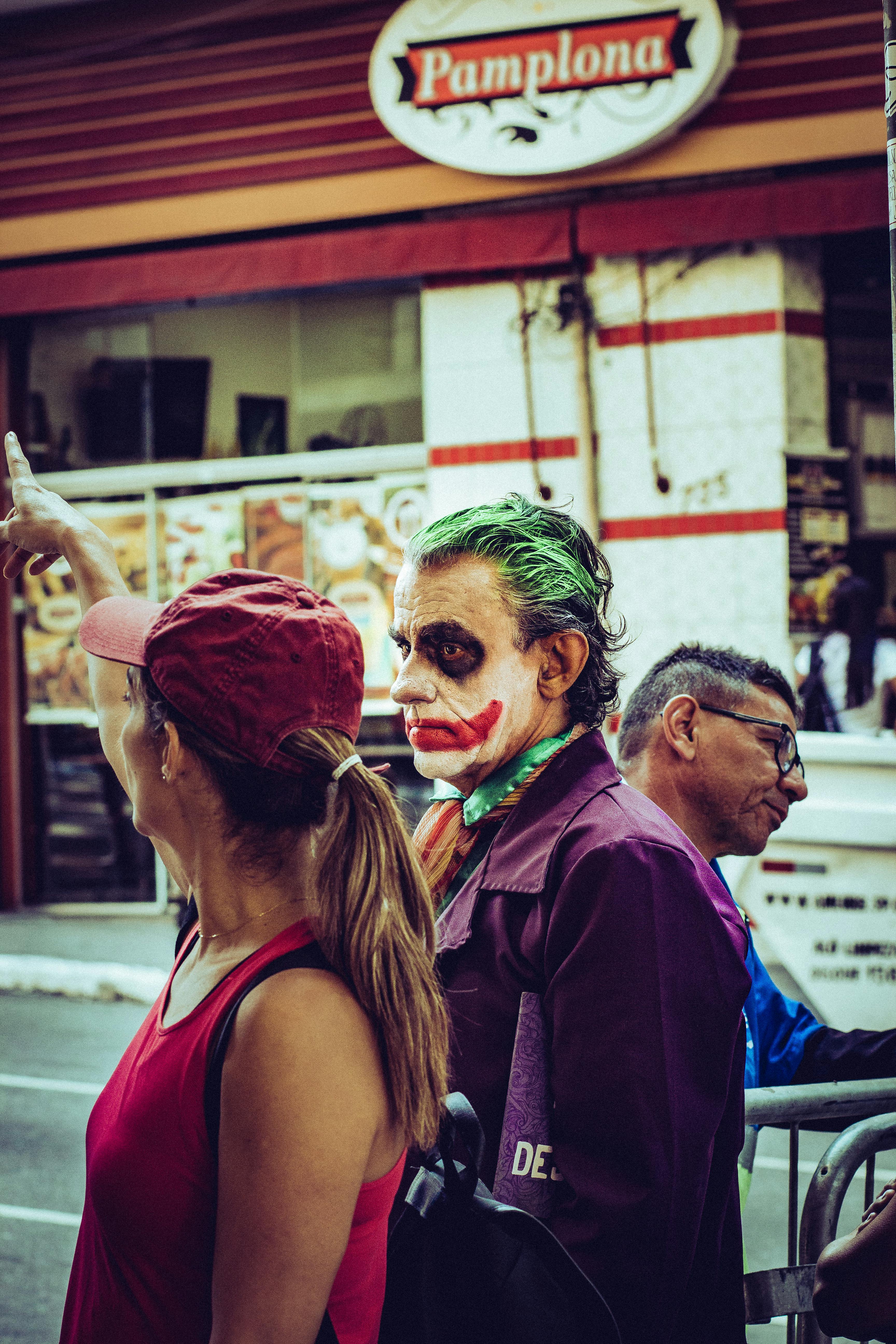 man in joker costume standing beside woman in red cap