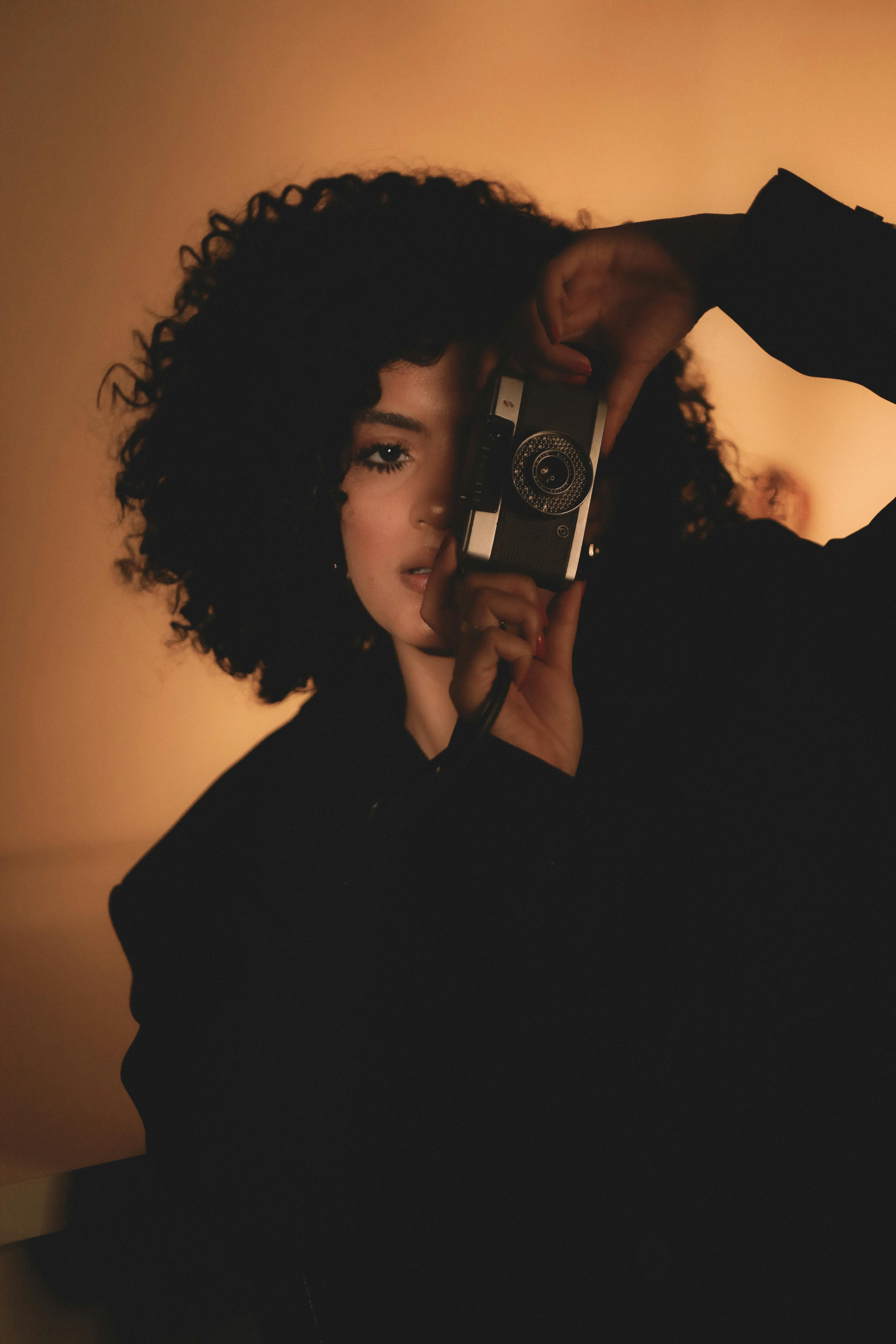Moody portrait of a woman using a vintage camera in soft lighting.