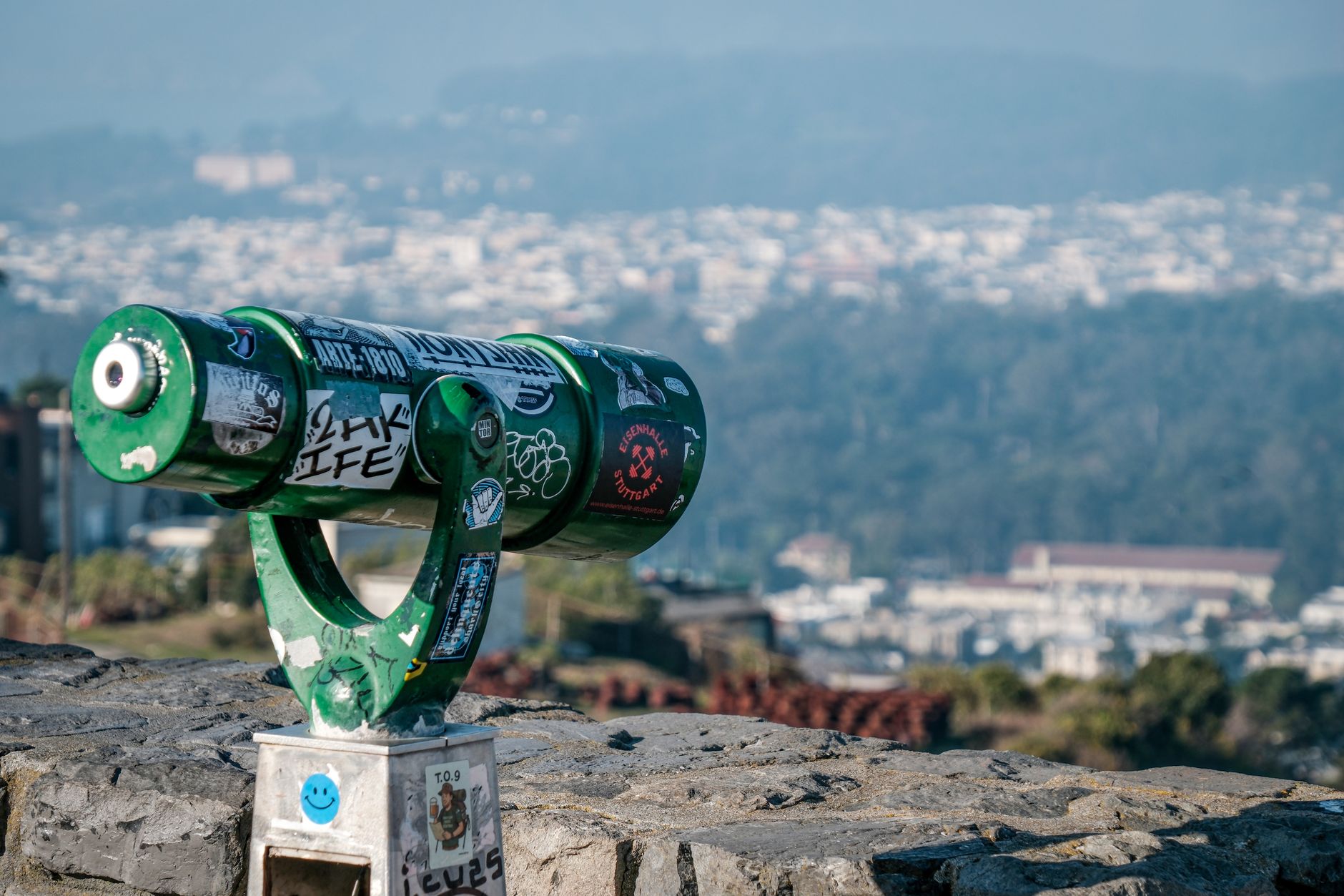 Green public binoculars overlooking a cityscape, offering a scenic urban view.
