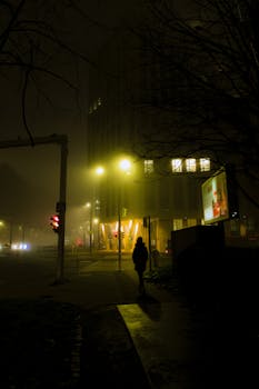 A solitary figure walks through a foggy, illuminated street in Bratislava at night.