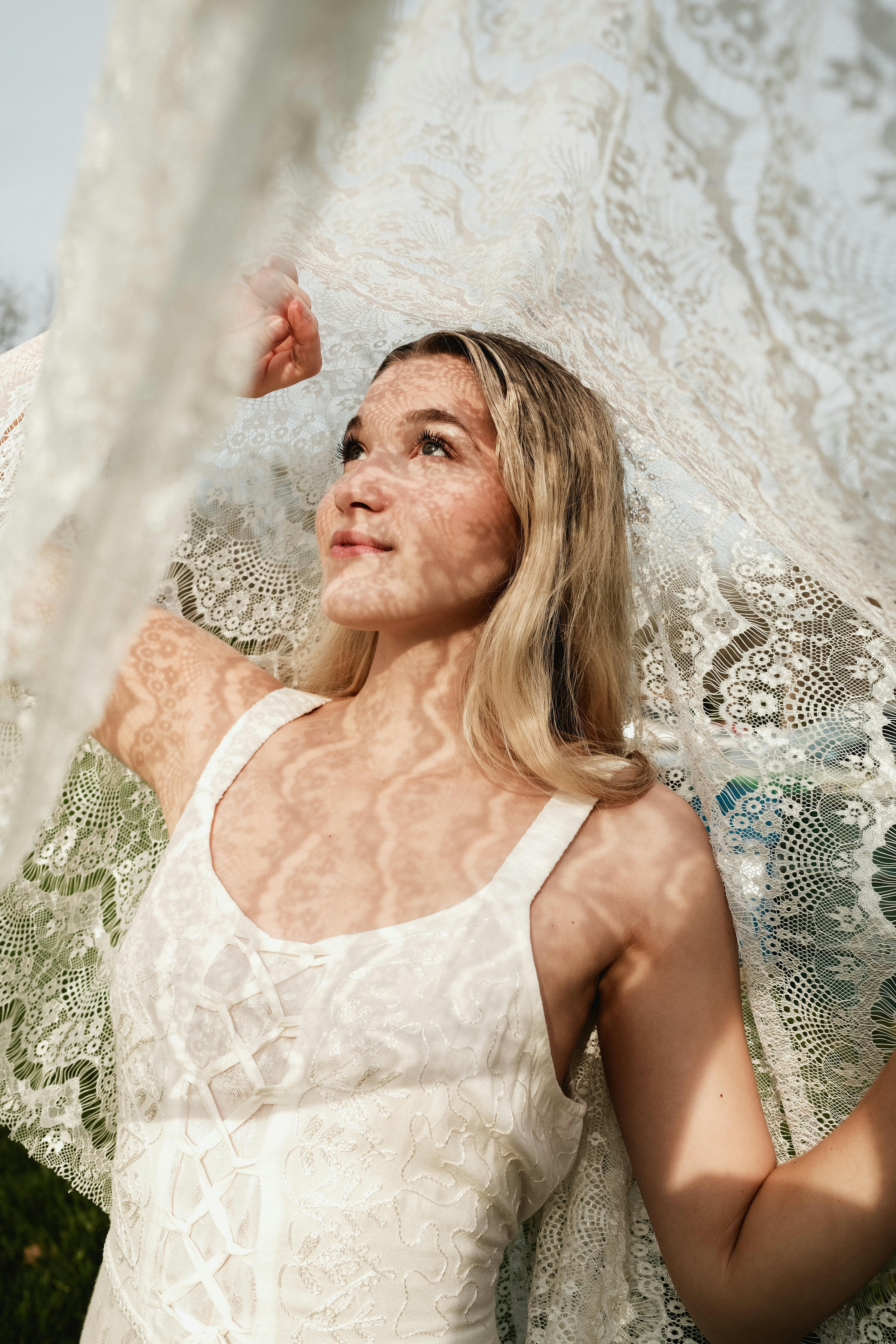 A bride stands under a delicate lace veil, casting intricate shadows in sunlight.