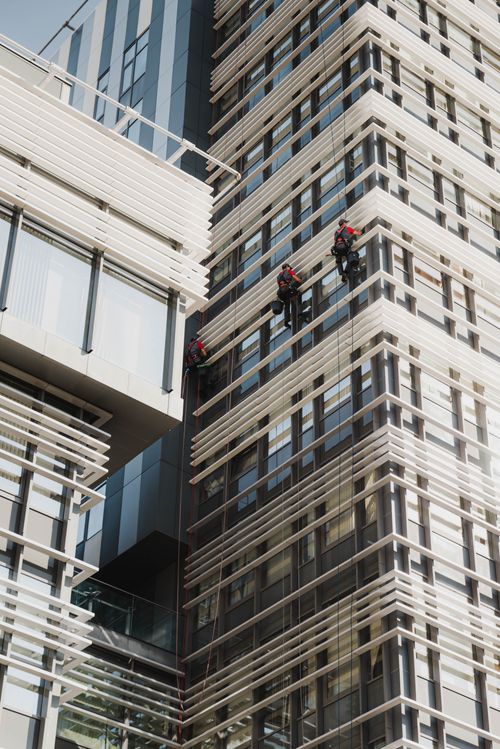 Free Tall modern skyscraper with window cleaners working on the glass facade in daylight. Stock Photo
