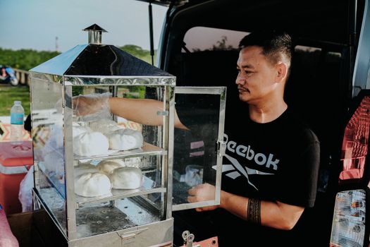 A street vendor selling steamed buns from a food stall at an outdoor market.