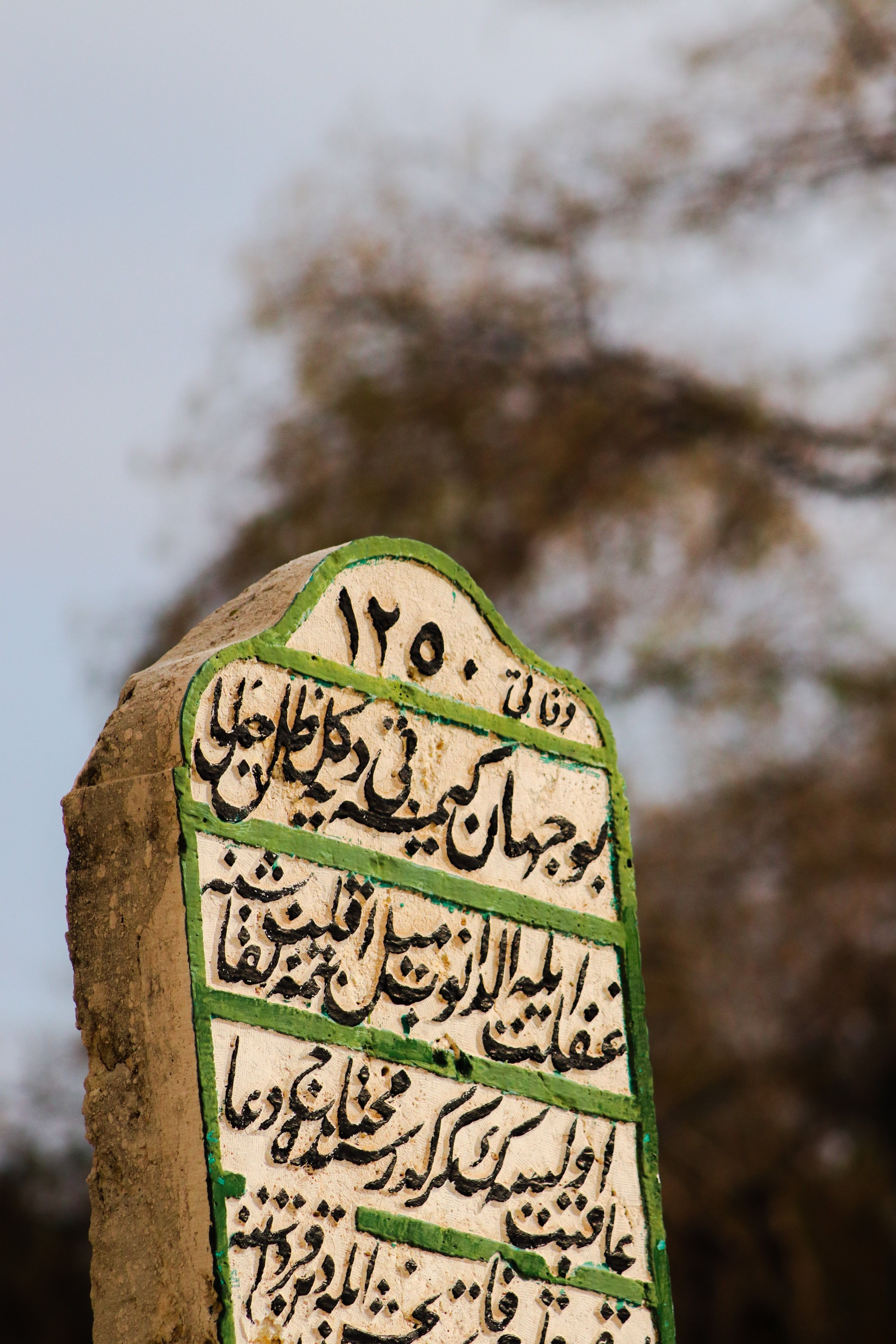 Close-up of a weathered stone marker with Arabic script, outdoors.