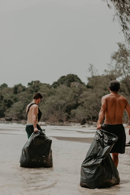 Shirtless men with trash bags on seashore