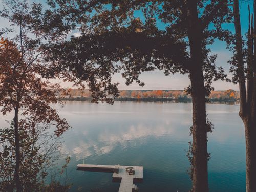 Free A serene lake scene during fall with vibrant foliage and a wooden dock under a clear blue sky. Stock Photo