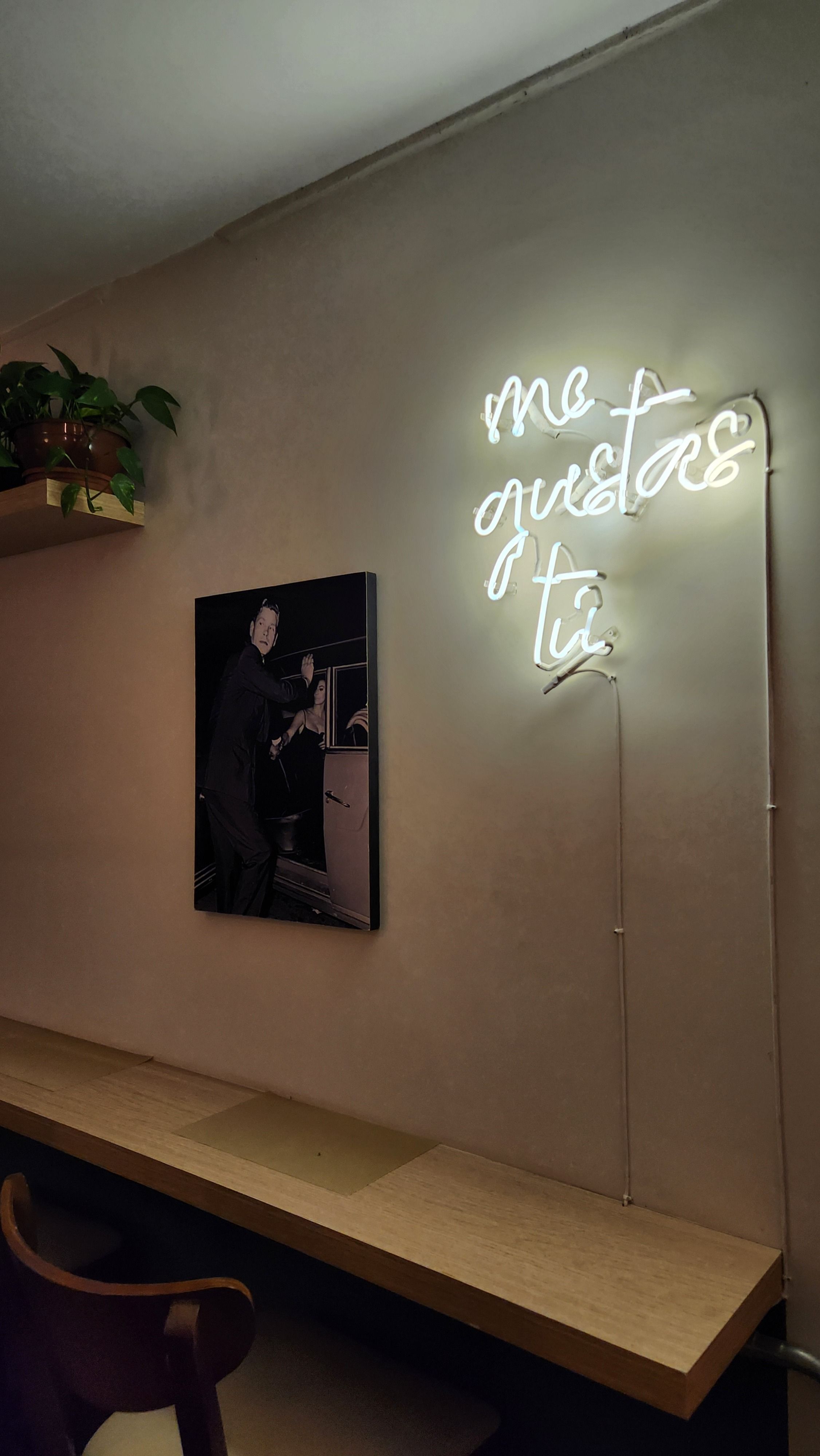 A cozy café interior in Curitiba with a glowing 'me gustas tú' neon sign and artwork on the wall.