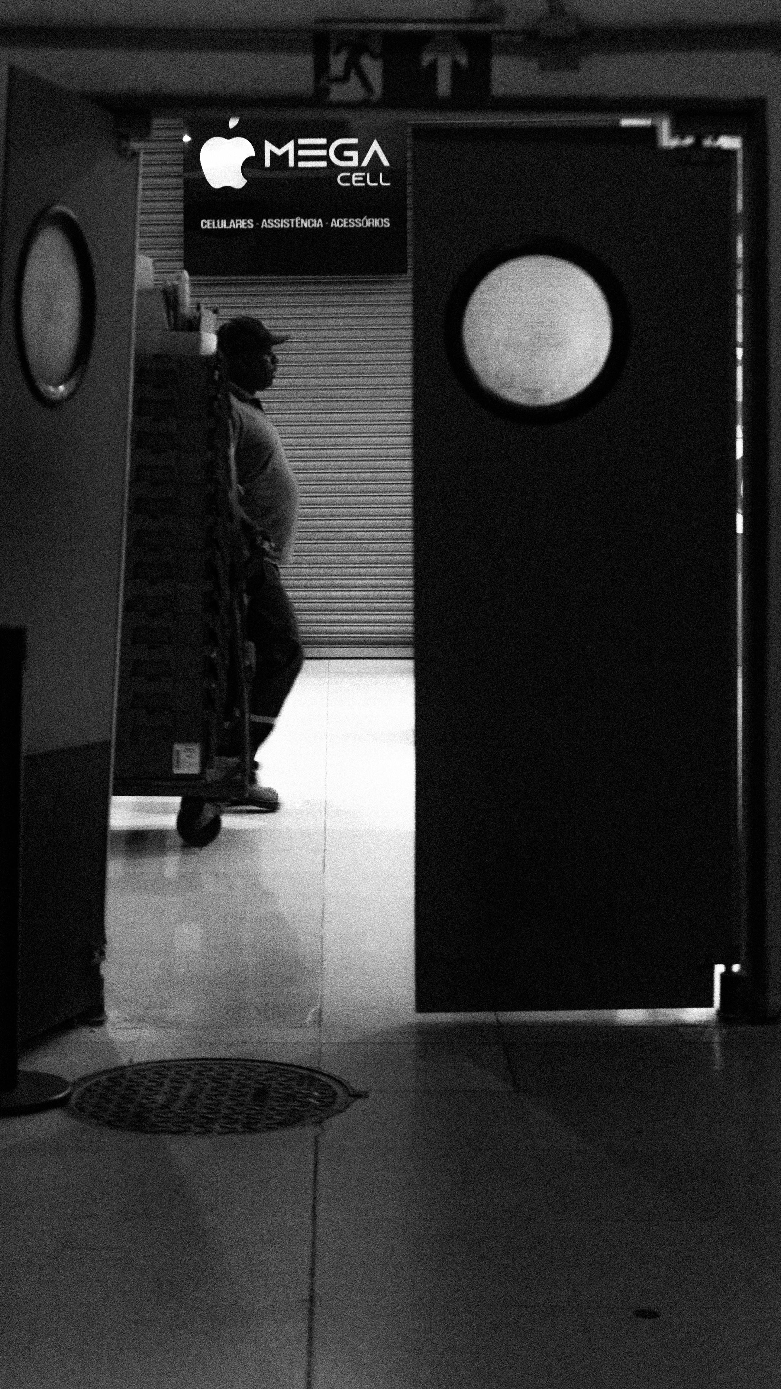 Gratis Immagine in bianco e nero di un lavoratore in piedi dietro la porta di un magazzino parzialmente aperta. Foto a disposizione