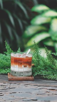 Glass of iced coffee placed on a table surrounded by lush green plants, conveying a refreshing outdoor feel.