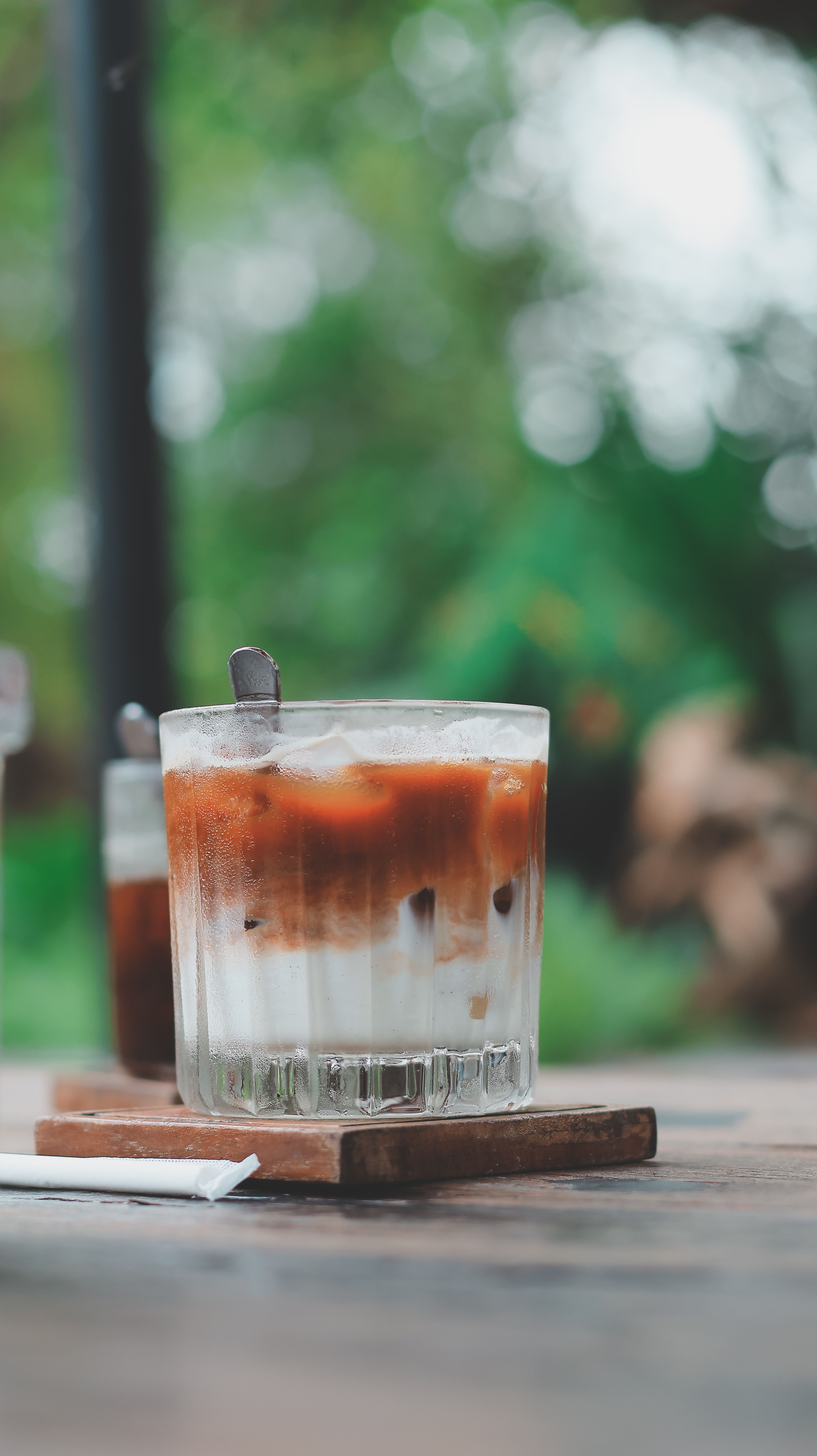 A refreshing iced coffee served in a glass with a straw on a wooden table outdoors.