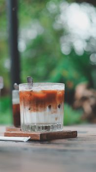 A refreshing iced coffee served in a glass with a straw on a wooden table outdoors.