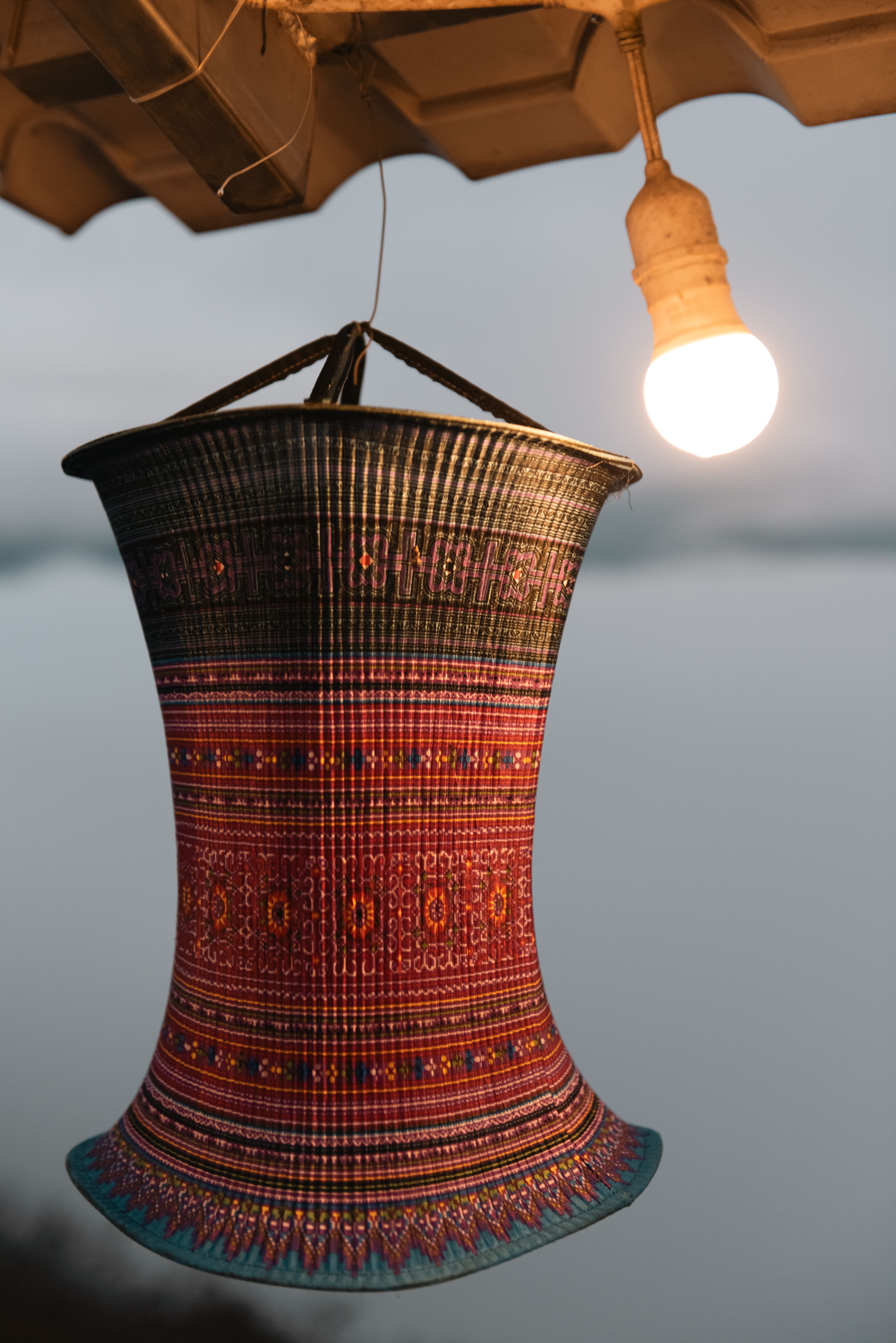 A woven Vietnamese basket with intricate patterns hangs under a glowing lightbulb.