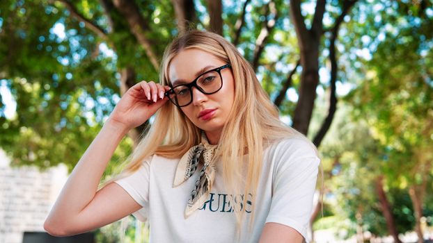 Fashionable woman in glasses poses outdoors, showcasing casual style.