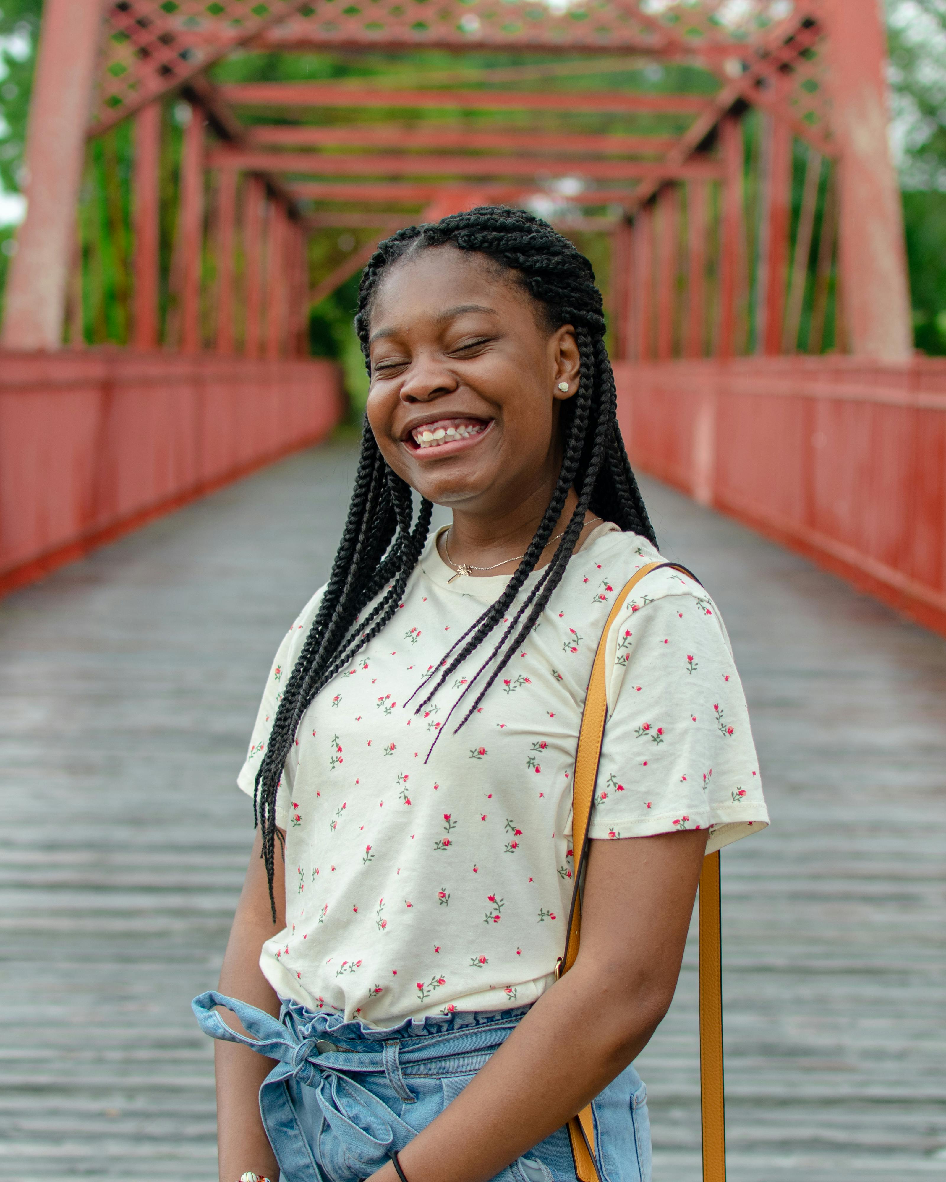 一位扎着辫子的年轻女子，穿着休闲花卉上衣，在红桥上快乐地微笑