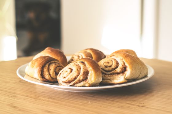 Plate of pinched cinnamon buns showing brown swirled spirals on a wooden table