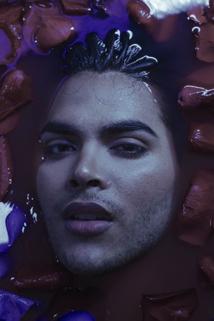 Moody portrait of a man immersed in water with rose petals around.