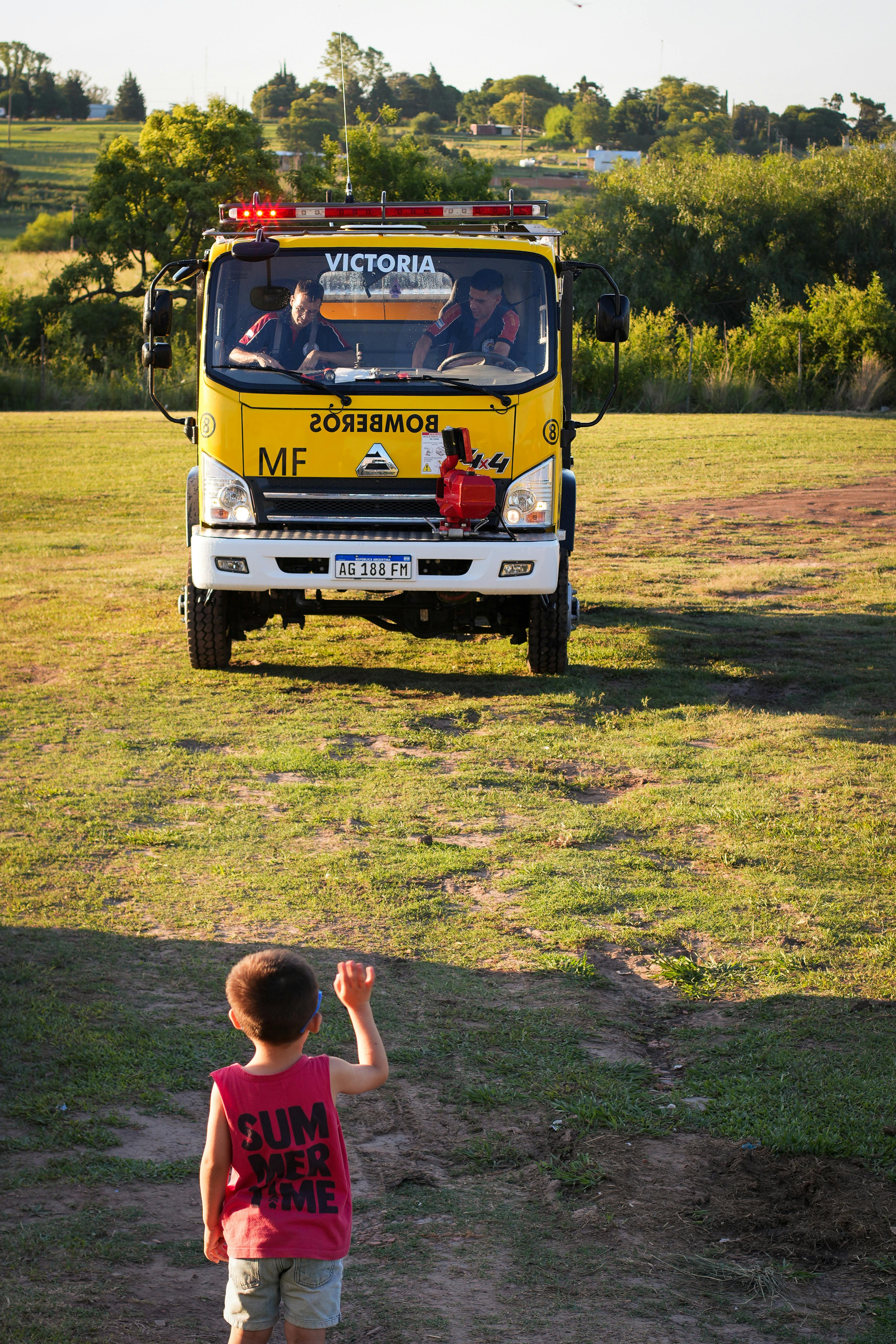A young boy waves at a fire truck in a grassy field in Entre Ríos, Argentina.