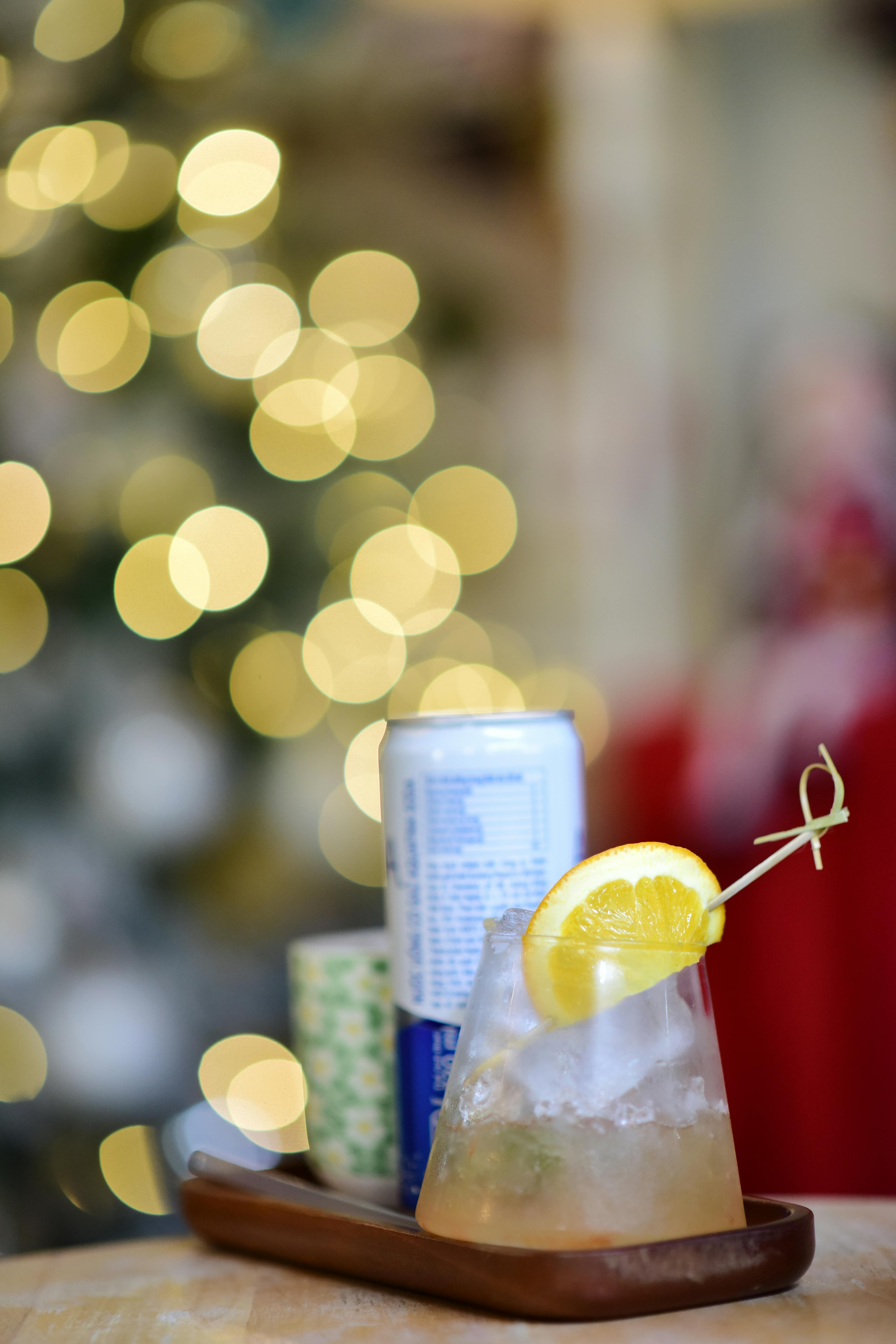 Artistic cocktail presentation with lemon garnish and festive bokeh lights background. Perfect for holiday themes.
