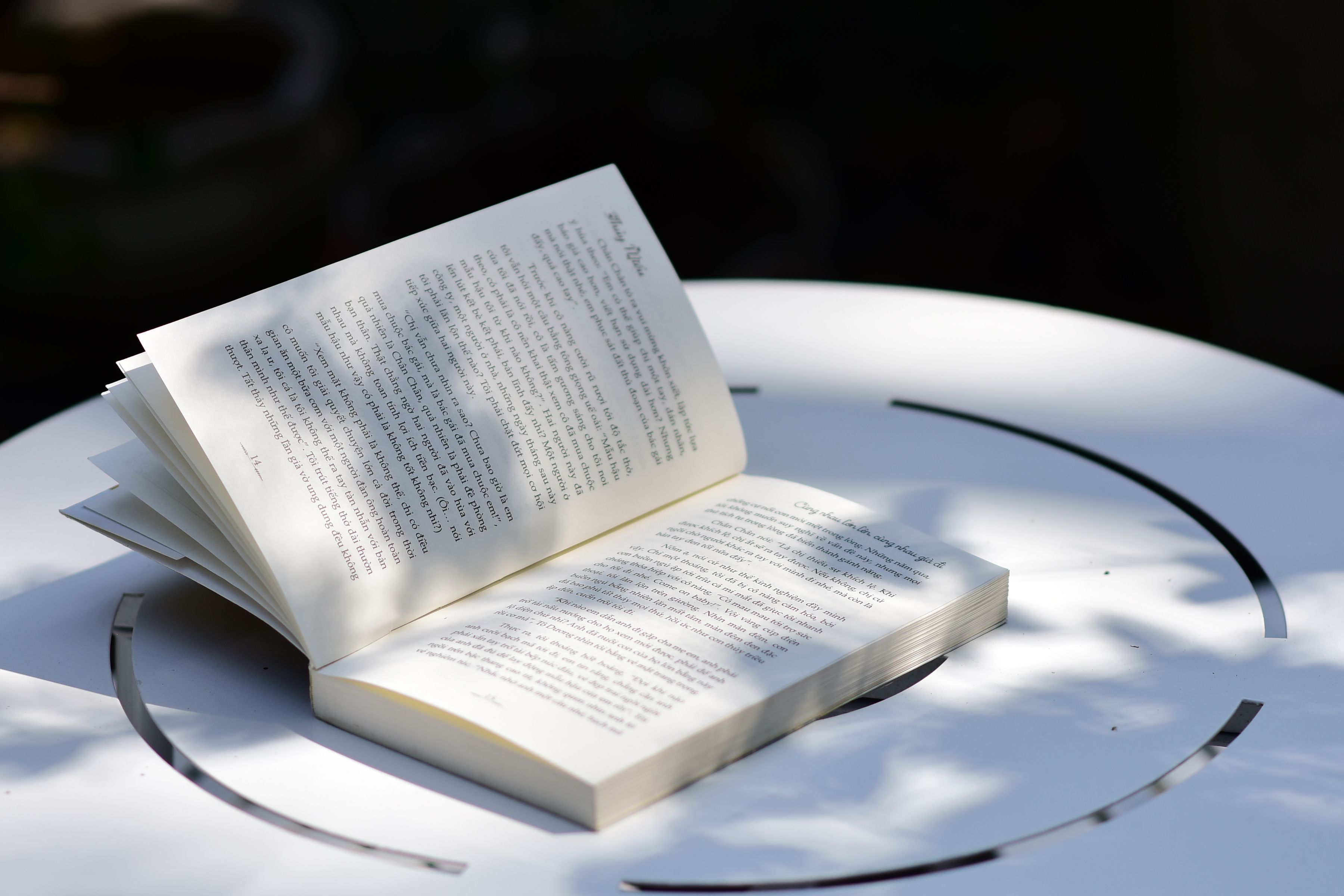 Open book on a white table with sunlit shadows, evoking a peaceful reading atmosphere outdoors.