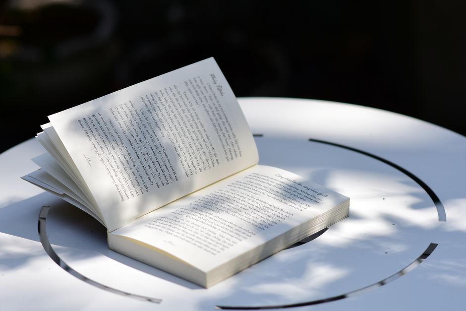 Open book on a white table with sunlit shadows, evoking a peaceful reading atmosphere outdoors.