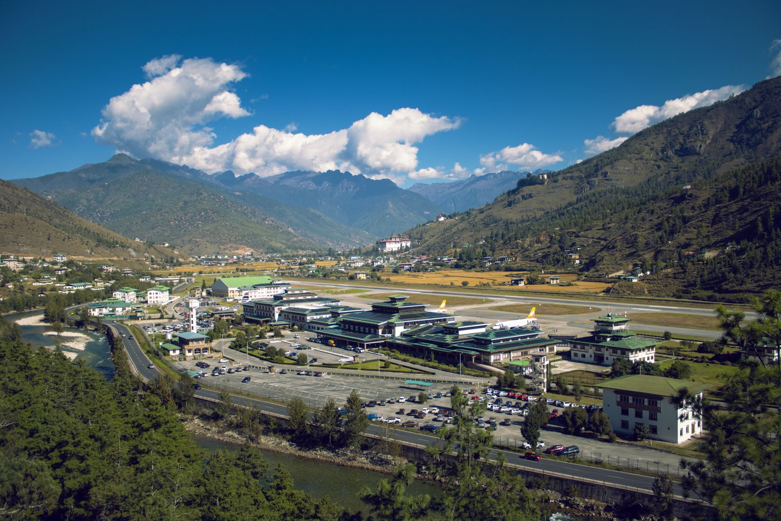 Paro airport seen from the hillside above, two jets at the green roofed terminal and the runway along the valley floor