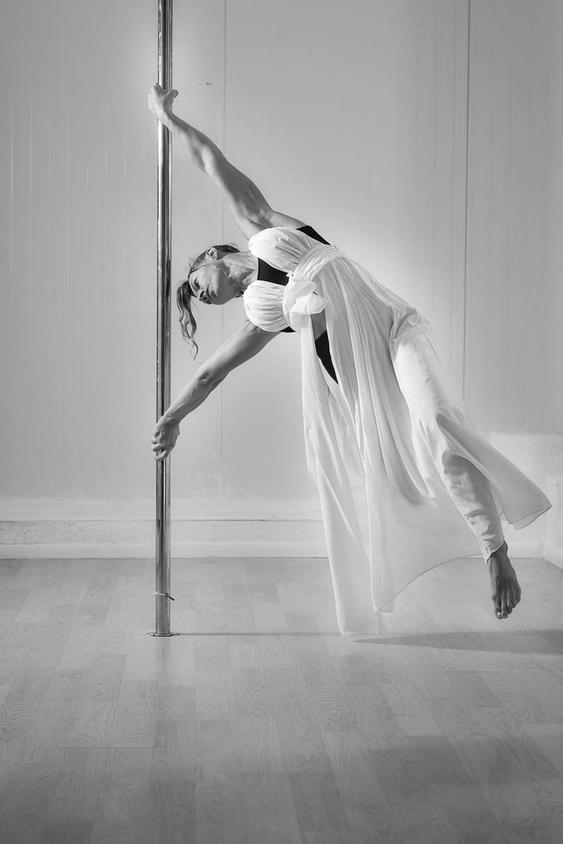 Elegant pole dancer in white dress showcasing balance and strength