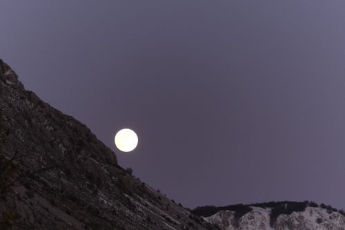 Free Captivating scene of a full moon rising over a rugged mountain ridge at twilight. Stock Photo