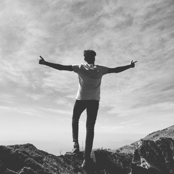 A black and white silhouette of a man raising arms triumphantly on a mountain peak.