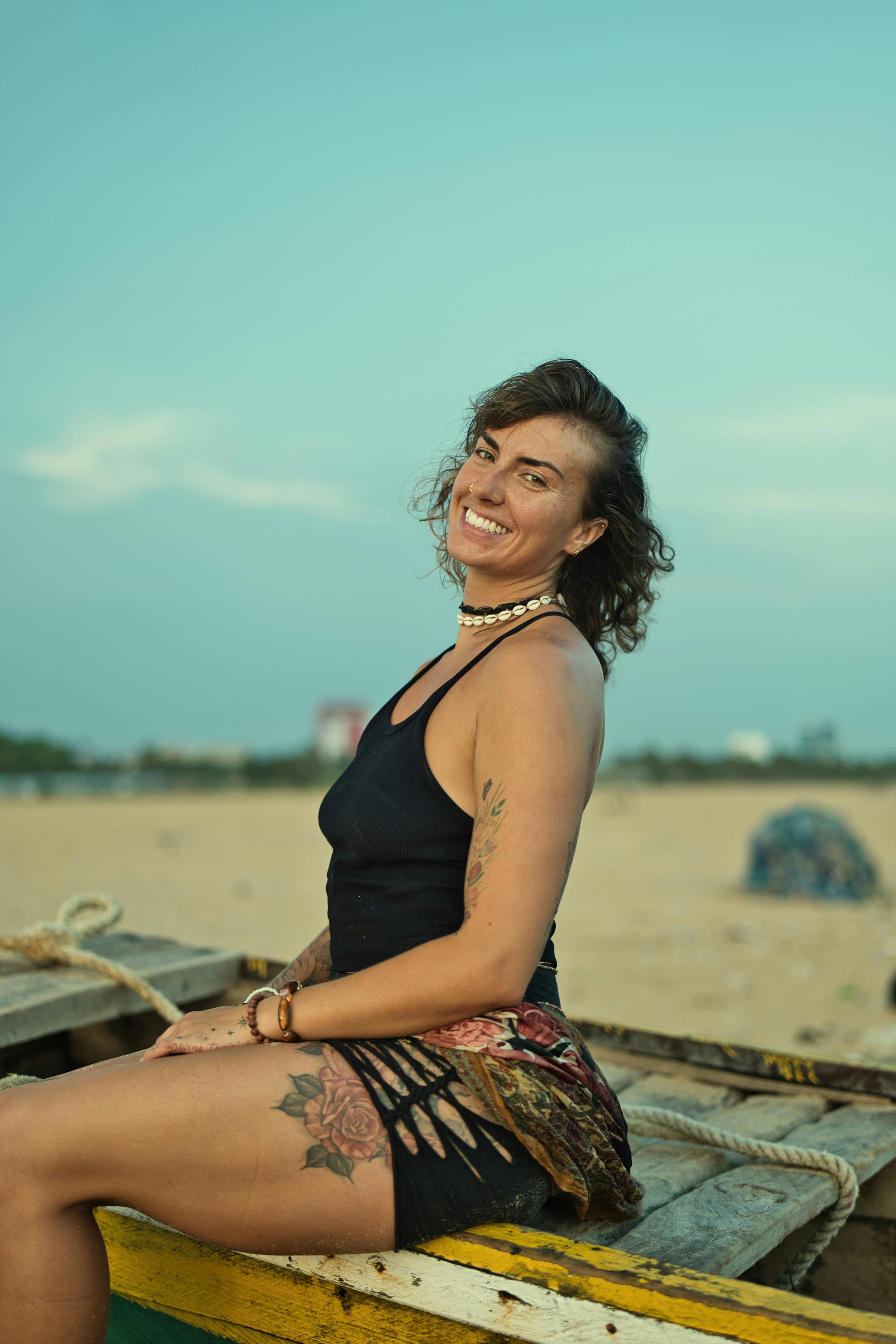 Relaxed woman with tattoos sitting on a boat by the beach during daytime.