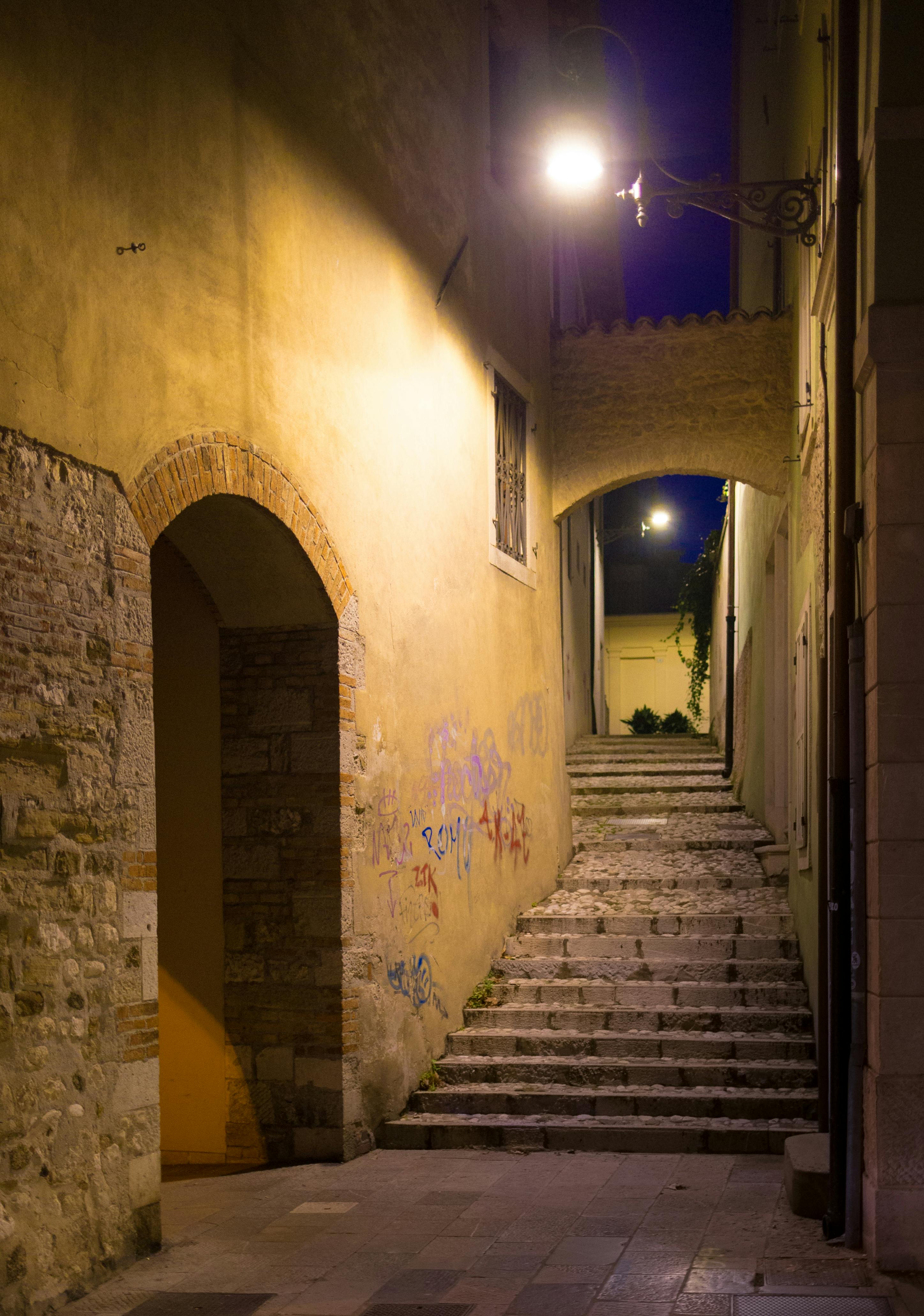Atmospheric narrow alleyway with steps and archway lit by night lights in Udine, Italy.