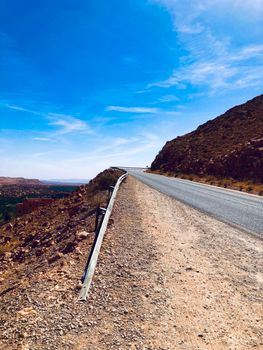 Lonely road stretching across desert landscape under a bright blue sky.
